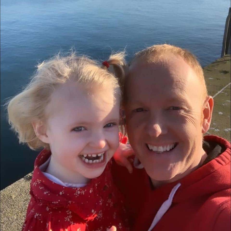Man and young child smiling together near the water.