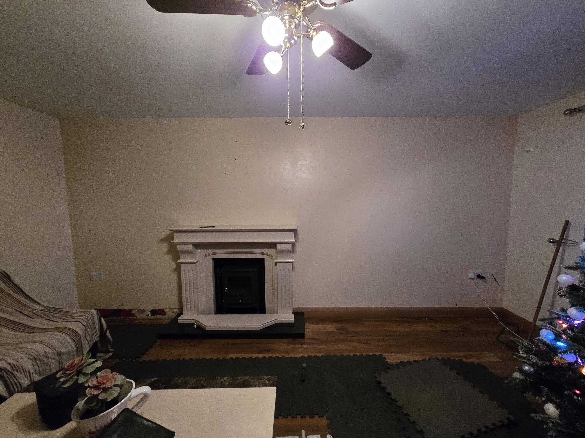 Living room with a ceiling fan, fireplace, striped chair, and Christmas tree decorated with lights.