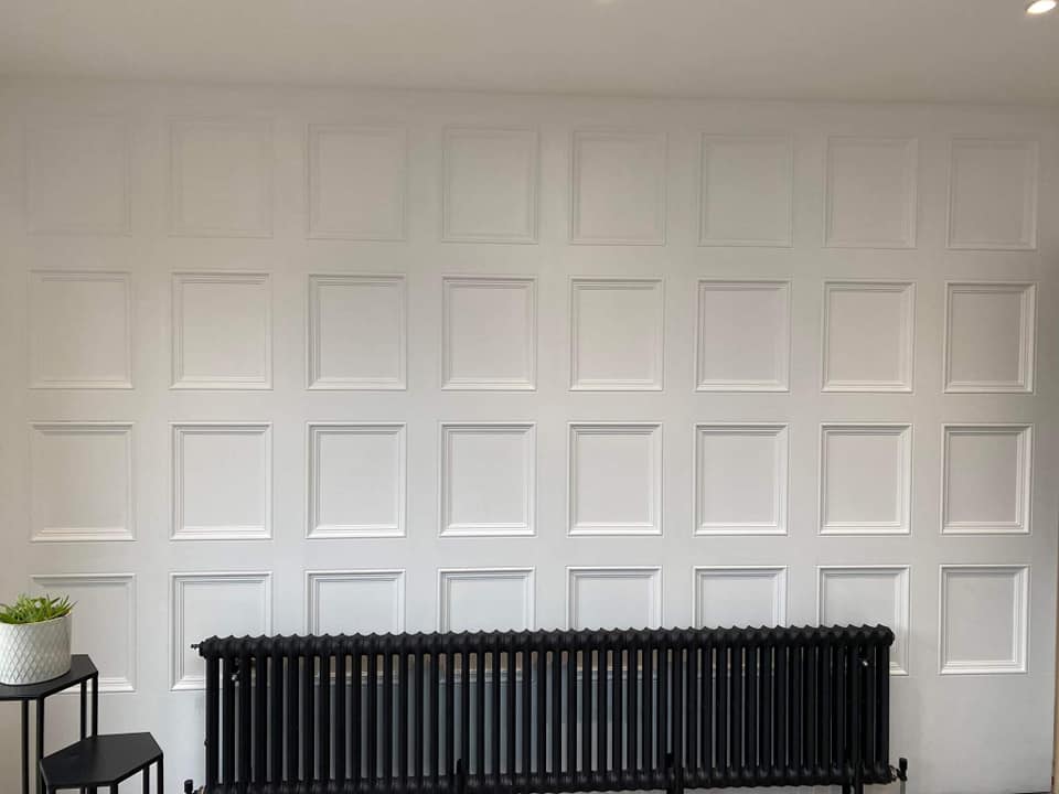 White paneled wall with a black radiator and a small table with a potted plant.