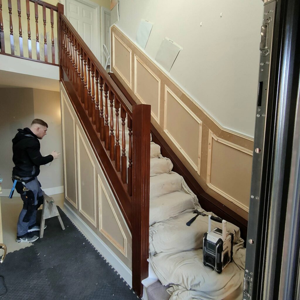 Man working on staircase renovation, with wooden panels and covered steps.
