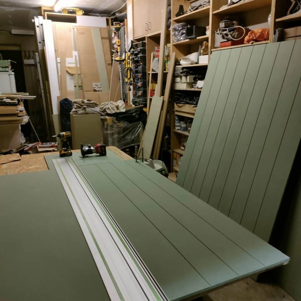 Workshop with tools, green panels, and shelving units filled with equipment and supplies.