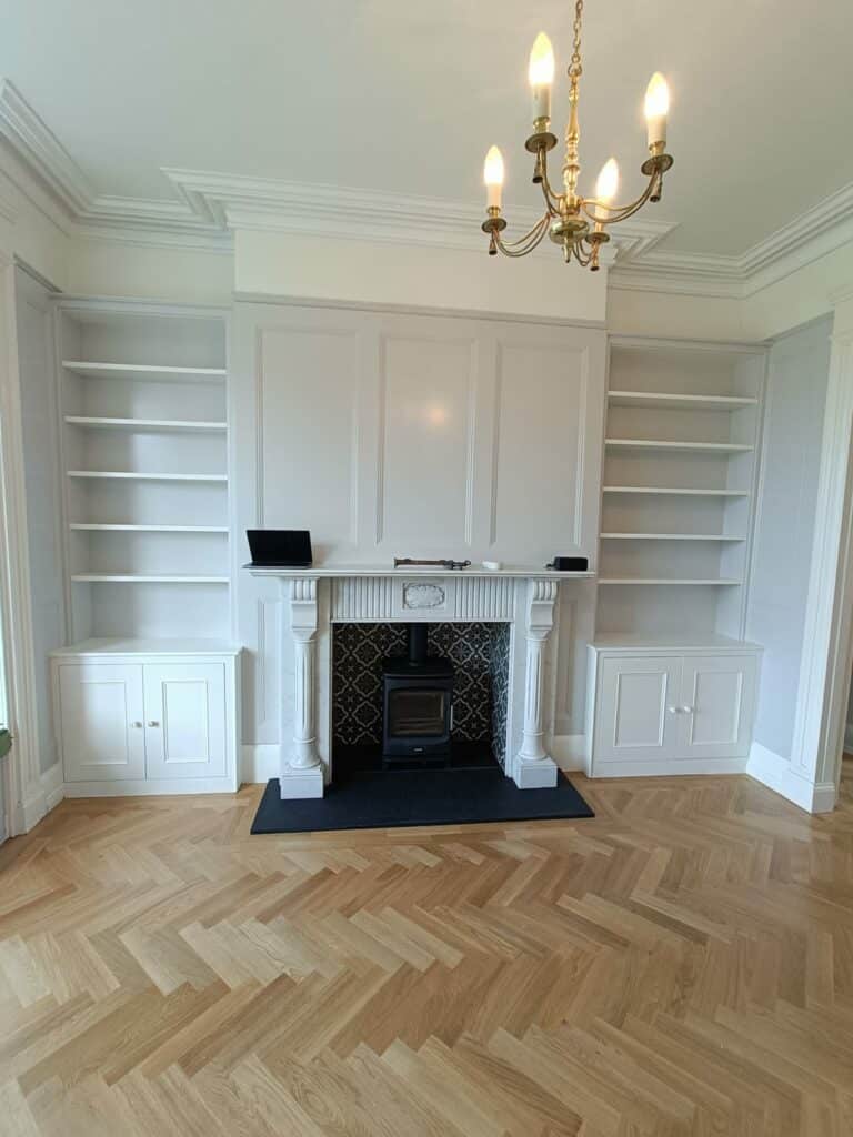 Elegant living room with white fireplace, built-in shelves, chandelier, and herringbone hardwood floor.
