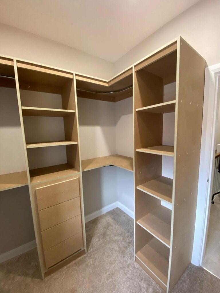 Empty wooden closet with shelves, drawers, and carpet flooring in a corner of a room.
