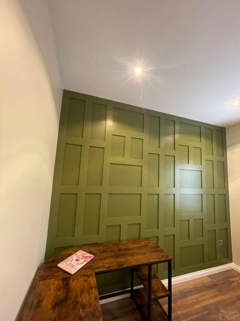 Green panel accent wall with geometric design and a wooden desk in a modern room.