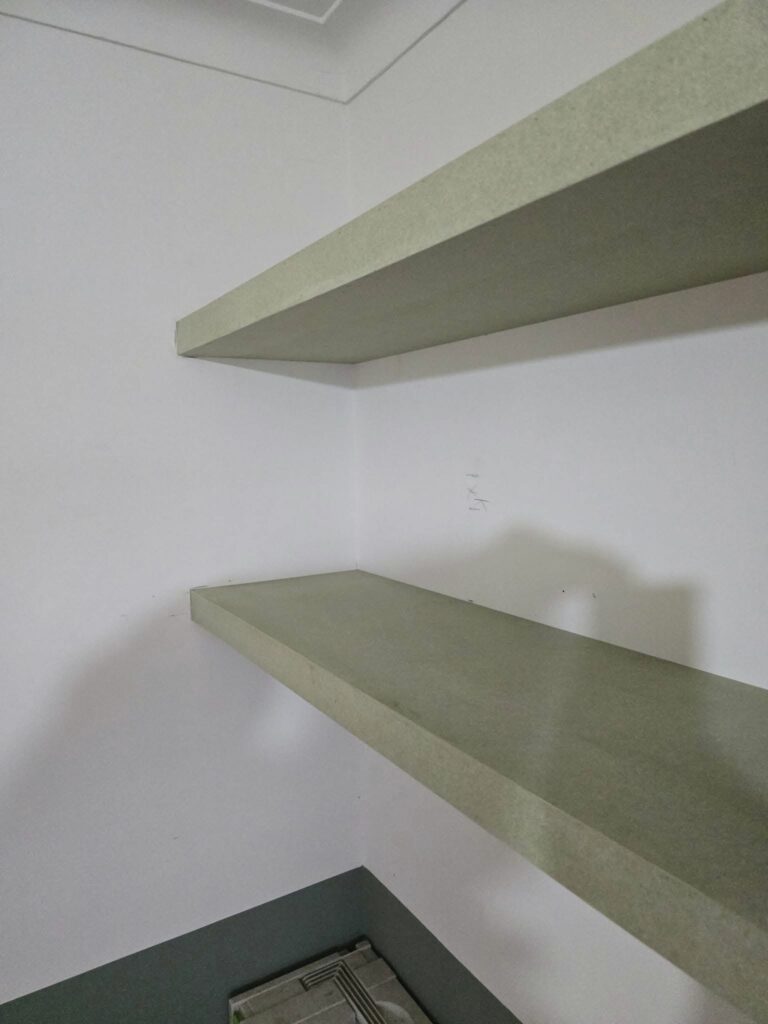 Corner of a room with two empty green shelves mounted on white walls.