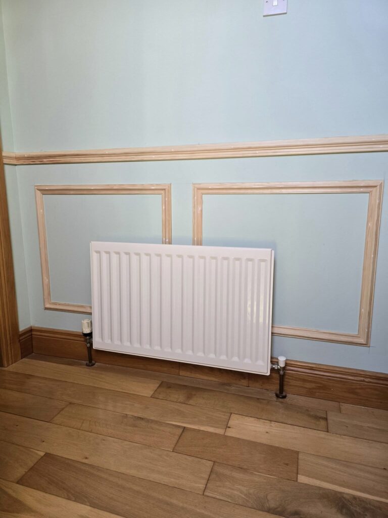 White radiator on a blue wall with wooden trim, above a wooden floor.
