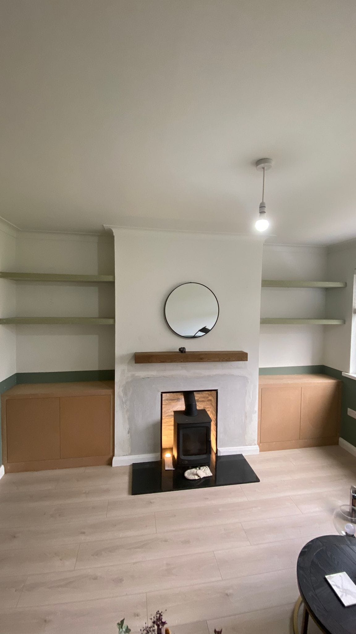 Minimalist living room with a wood stove, round mirror, and built-in shelves.