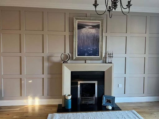Elegant living room with beige paneled walls, modern fireplace, framed artwork, and chandelier.