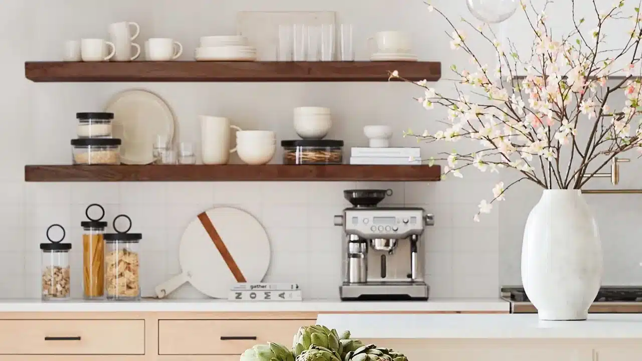 Modern kitchen with floating wooden shelves, ceramics, jars, espresso machine, and a large vase with flowers.