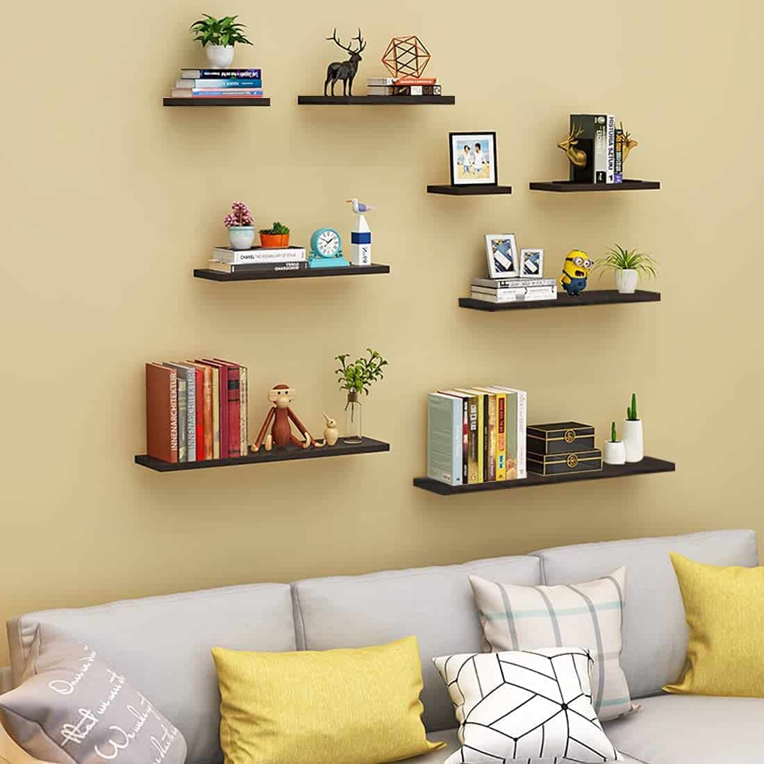 Floating shelves with books and decor on a beige wall above a sofa with colorful cushions.