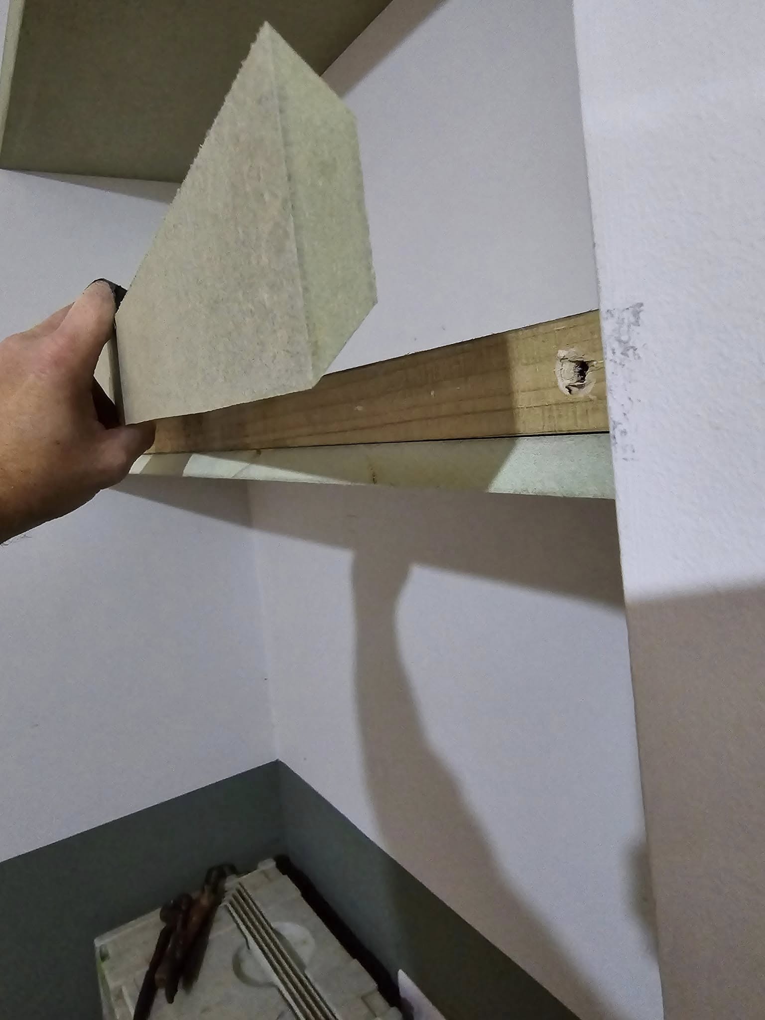 Hand installing a floating shelf on a wooden bracket in a corner wall.