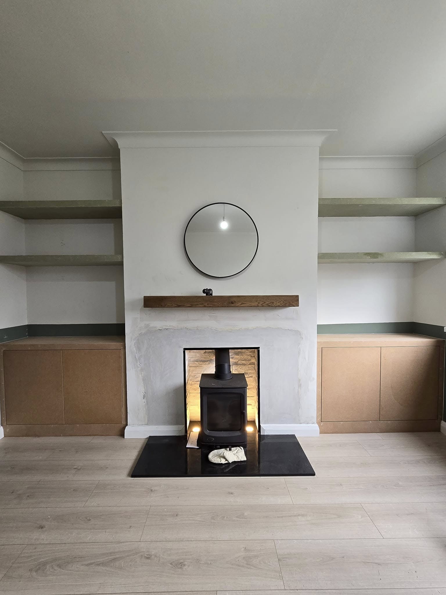 Living room with a modern fireplace, floating shelves, and a round mirror above the mantel.
