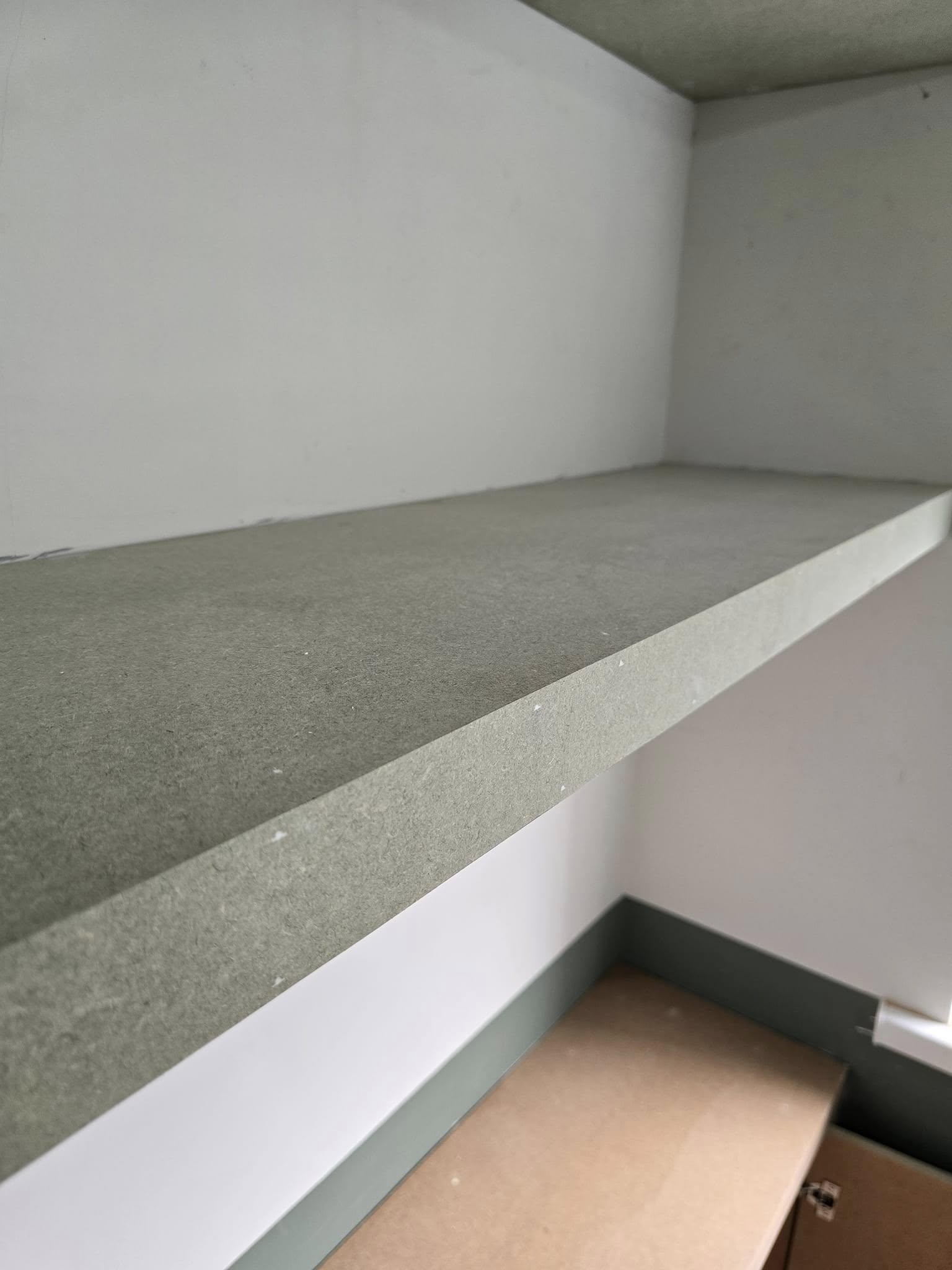 Close-up of a minimalist green floating shelf mounted on a white wall.