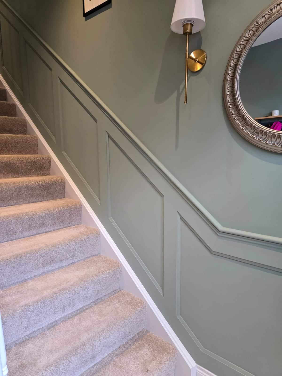 Staircase with beige carpet and green walls featuring framed mouldings and a decorative wall lamp.