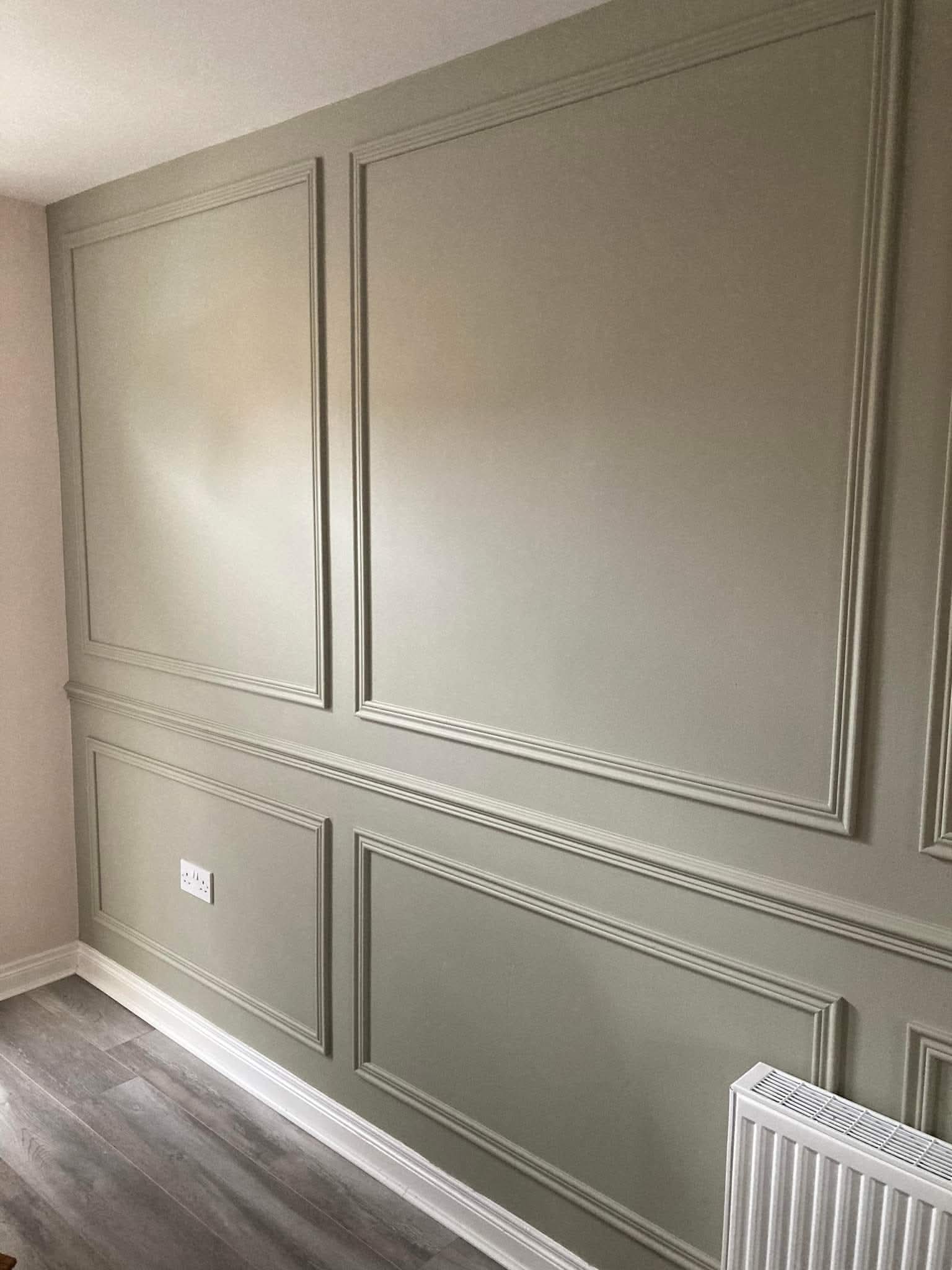 Green French-style wall paneling in a room with wooden flooring.