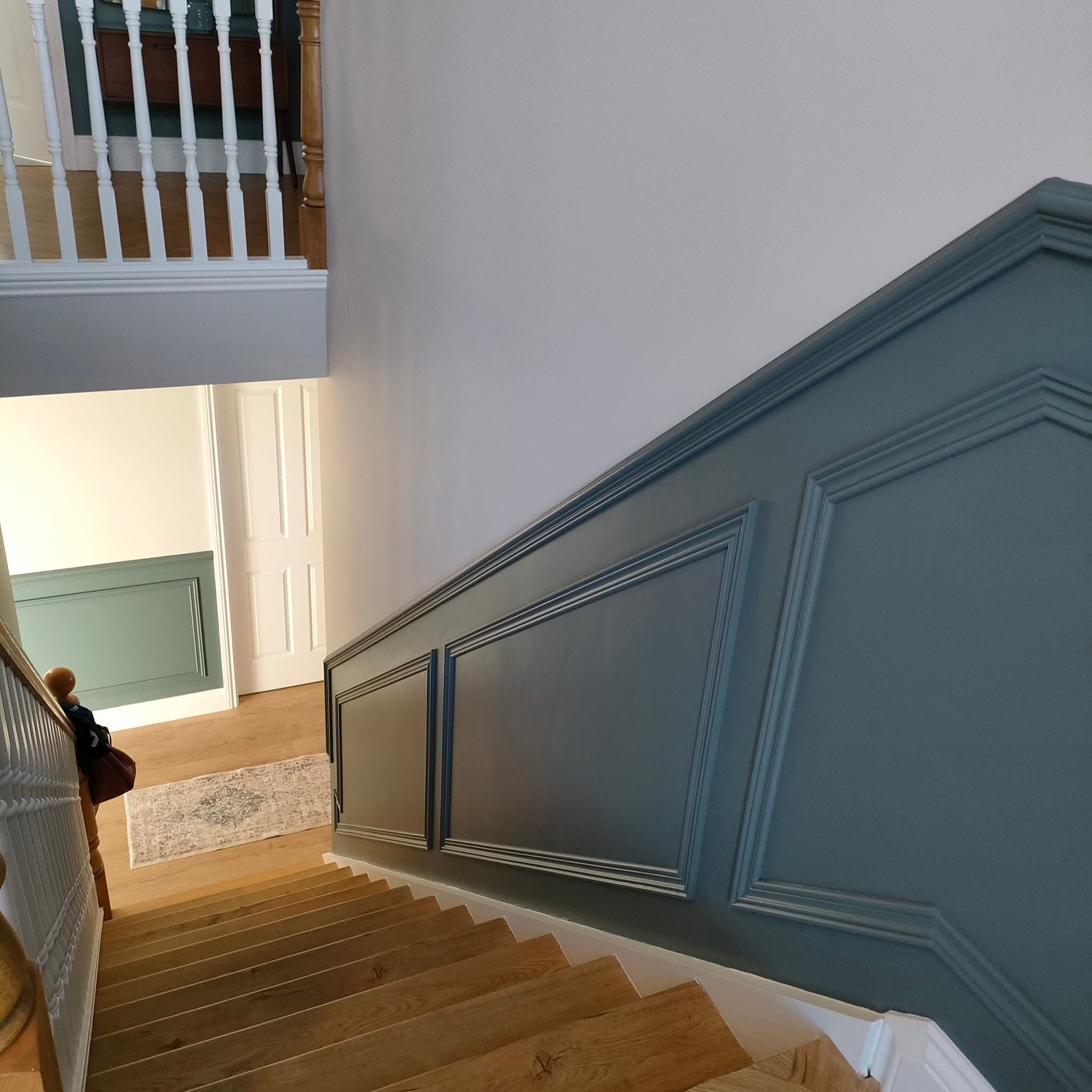 Elegant staircase with wooden steps and teal French panelling.