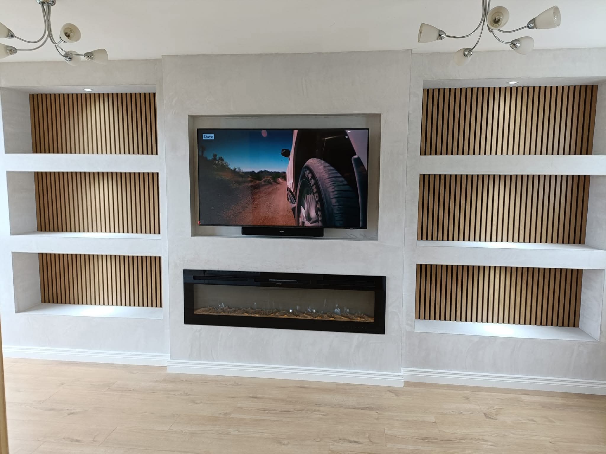 Modern living room wall with a TV, built-in shelves with wood slats, and an electric fireplace.