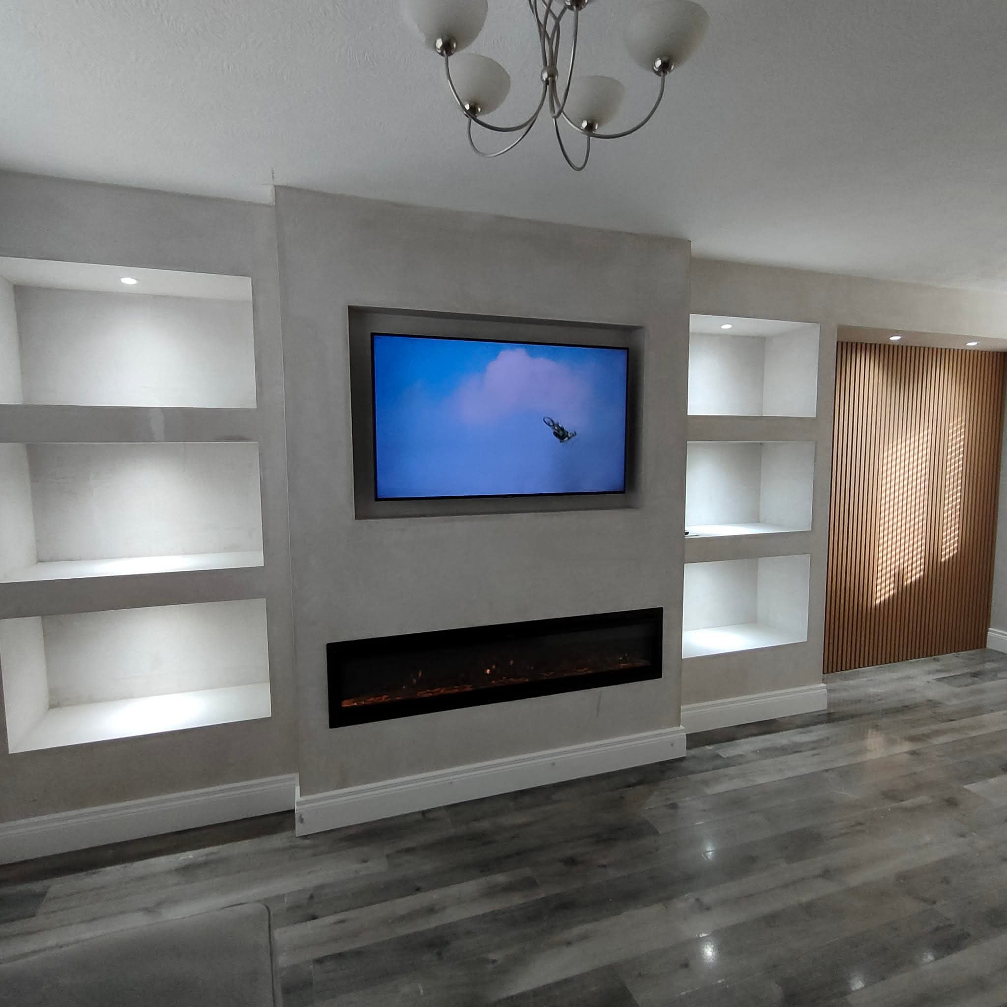 Modern living room with TV and fireplace integrated into a media wall, surrounded by illuminated shelves and wood paneling.