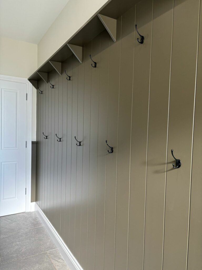 Tongue and groove style paneling with coat hooks and a white door.