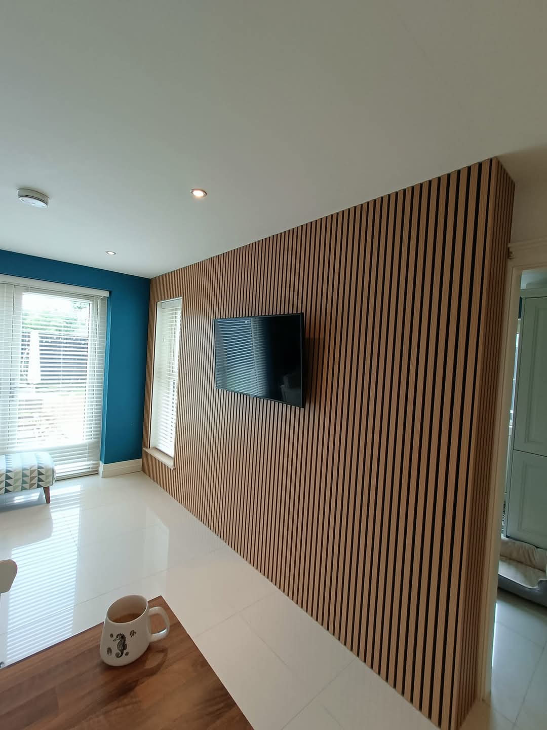 Modern room with an acoustic slat wall, mounted TV, and a window with blinds.