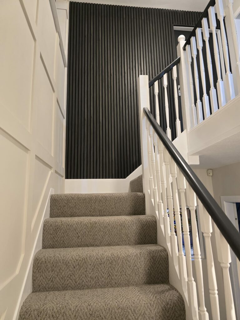 Carpeted staircase with white railings and a black vertical slat accent wall.