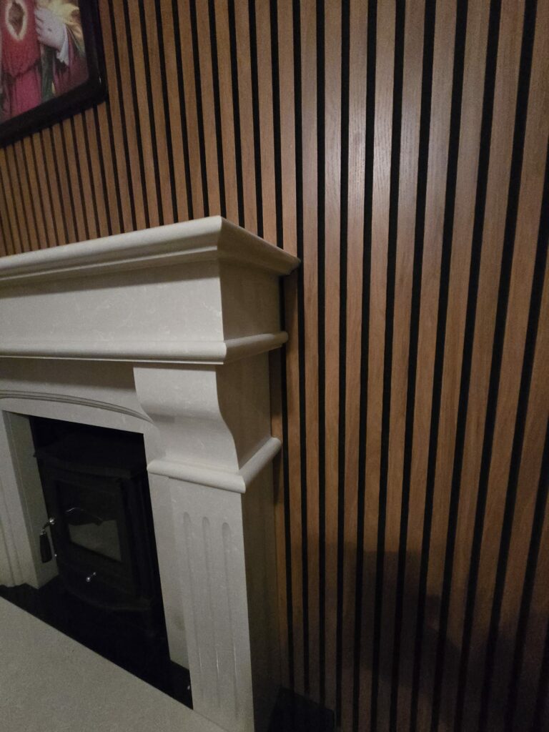 Fireplace with a white mantel against a wooden slat wall in a dimly lit room.