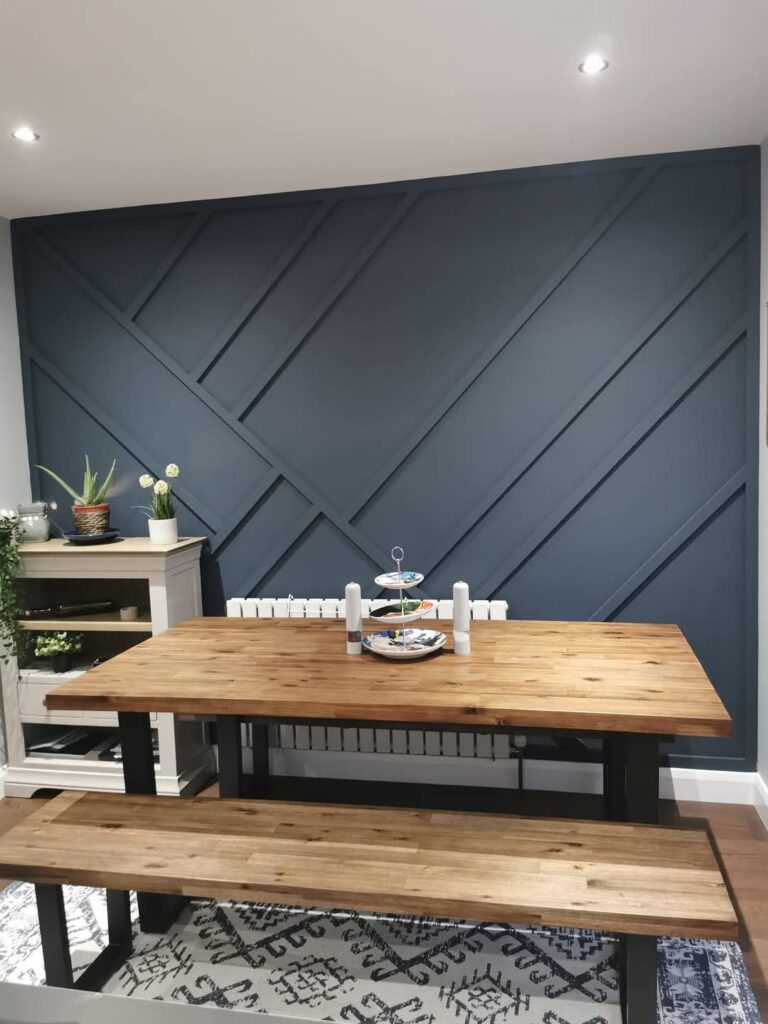 Dining room with wooden table, benches, modern blue accent wall, and decorative plants on a white cabinet.