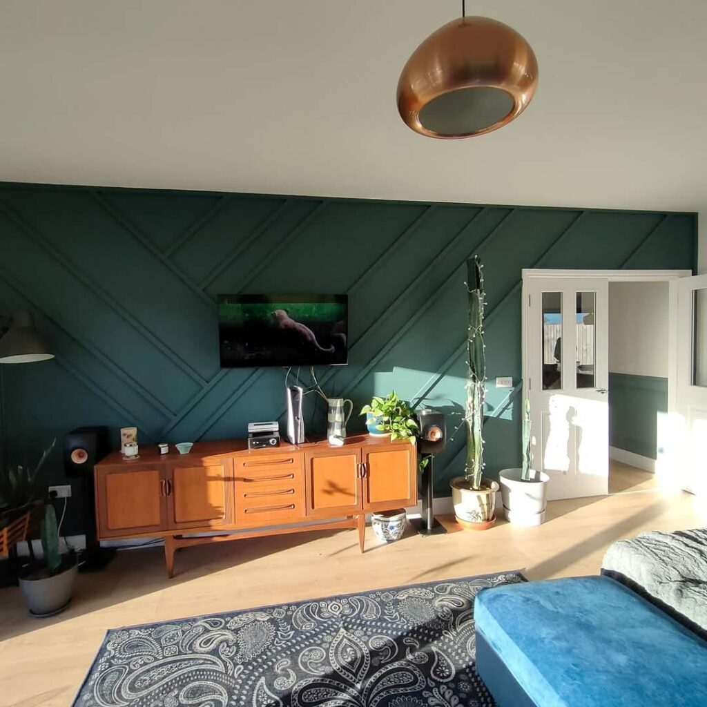 Modern living room with mid-century sideboard, green accent wall, wall-mounted TV, indoor plants, and blue upholstered furniture.