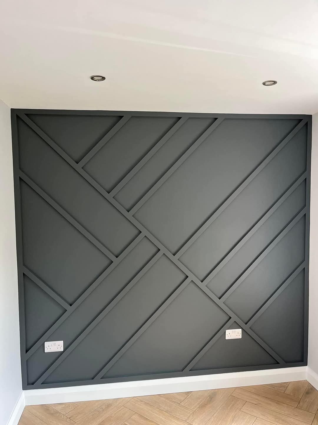 Geometric feature wall with dark intersecting lines, two power outlets, recessed ceiling lights, and wood flooring.