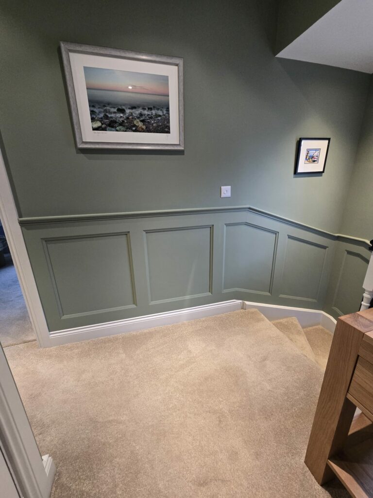 Hallway with green walls, framed landscape and small artwork, beige carpet, and wood accents.