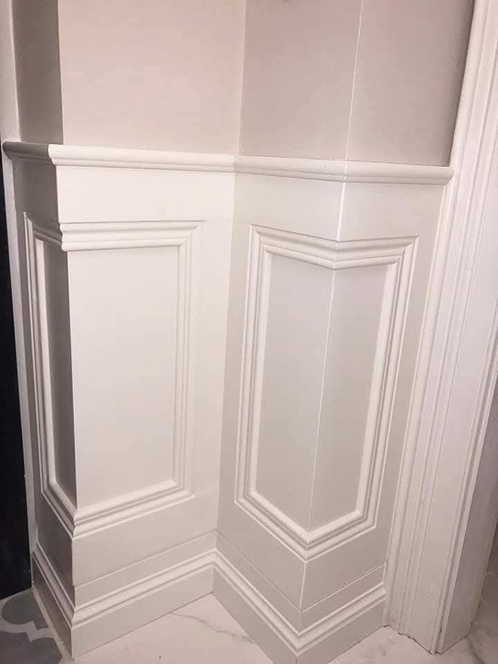White paneled wall with decorative moldings in a corner setting.