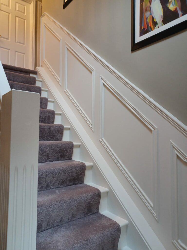 Carpeted staircase with white wainscoting and colorful wall art.