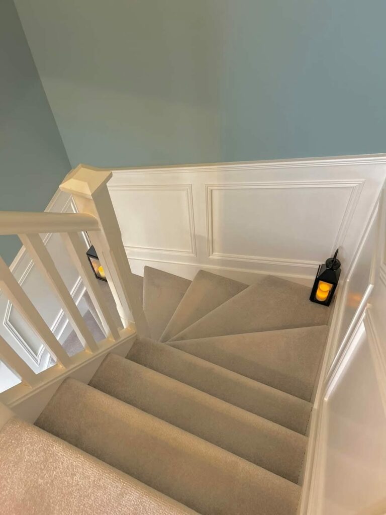 Carpeted staircase with white railing and walls, featuring decorative lanterns on each side.