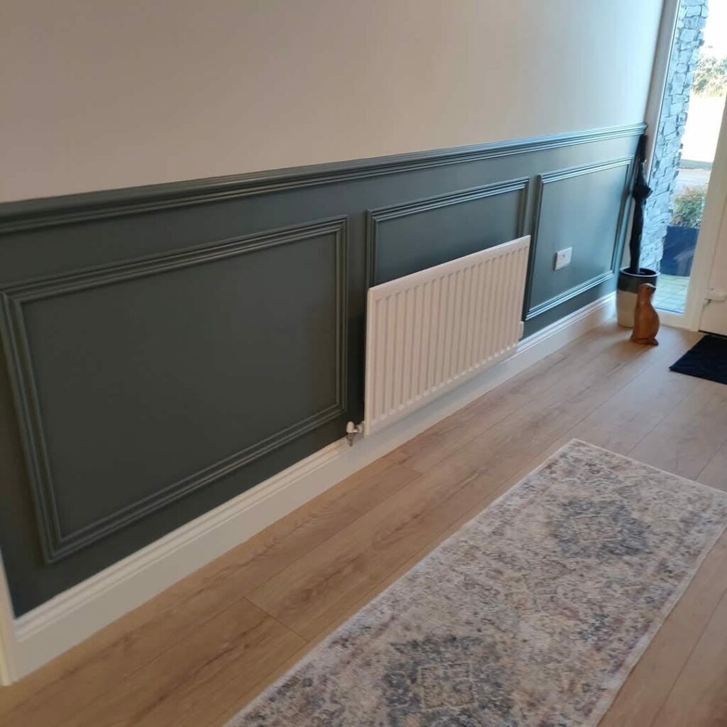 Hallway with green wainscoting, radiator, and wooden flooring; a rabbit sculpture near a glass door.