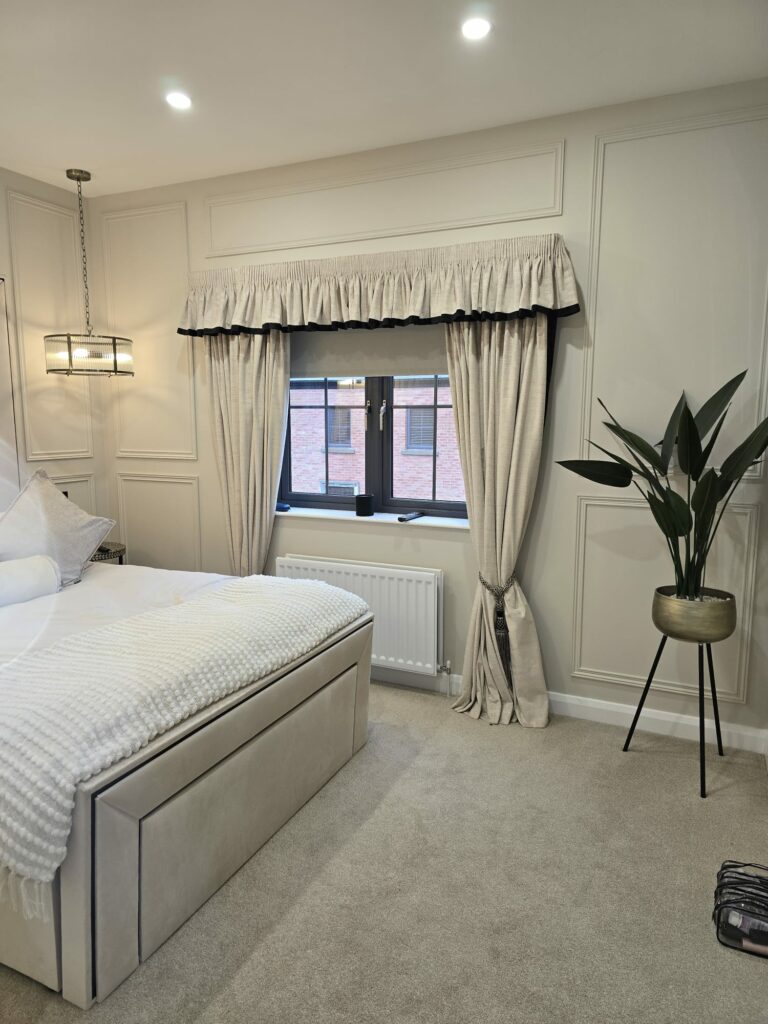 Elegant bedroom with beige curtains, a plush bed, pendant light, and a potted plant on a stand.