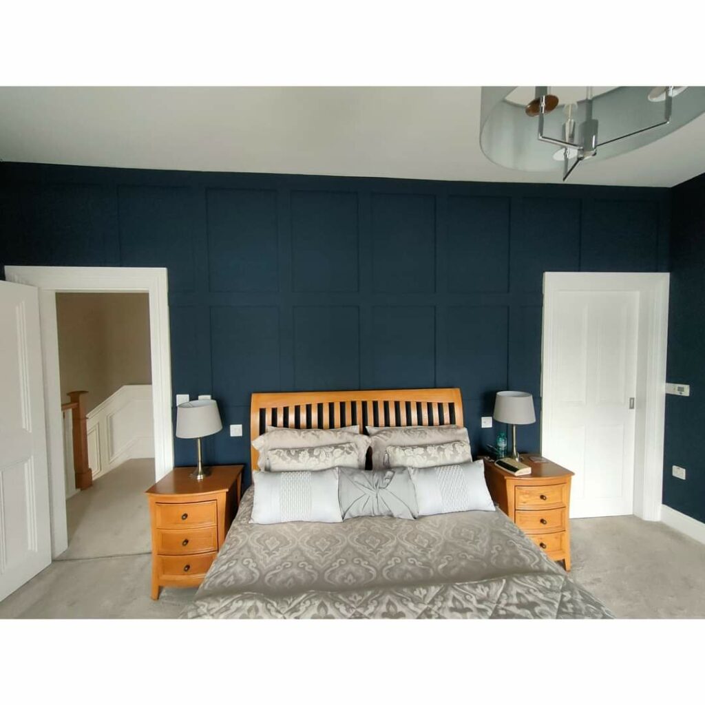 Bedroom with dark blue accent wall, wooden bed frame, matching nightstands, and ornate bedding.