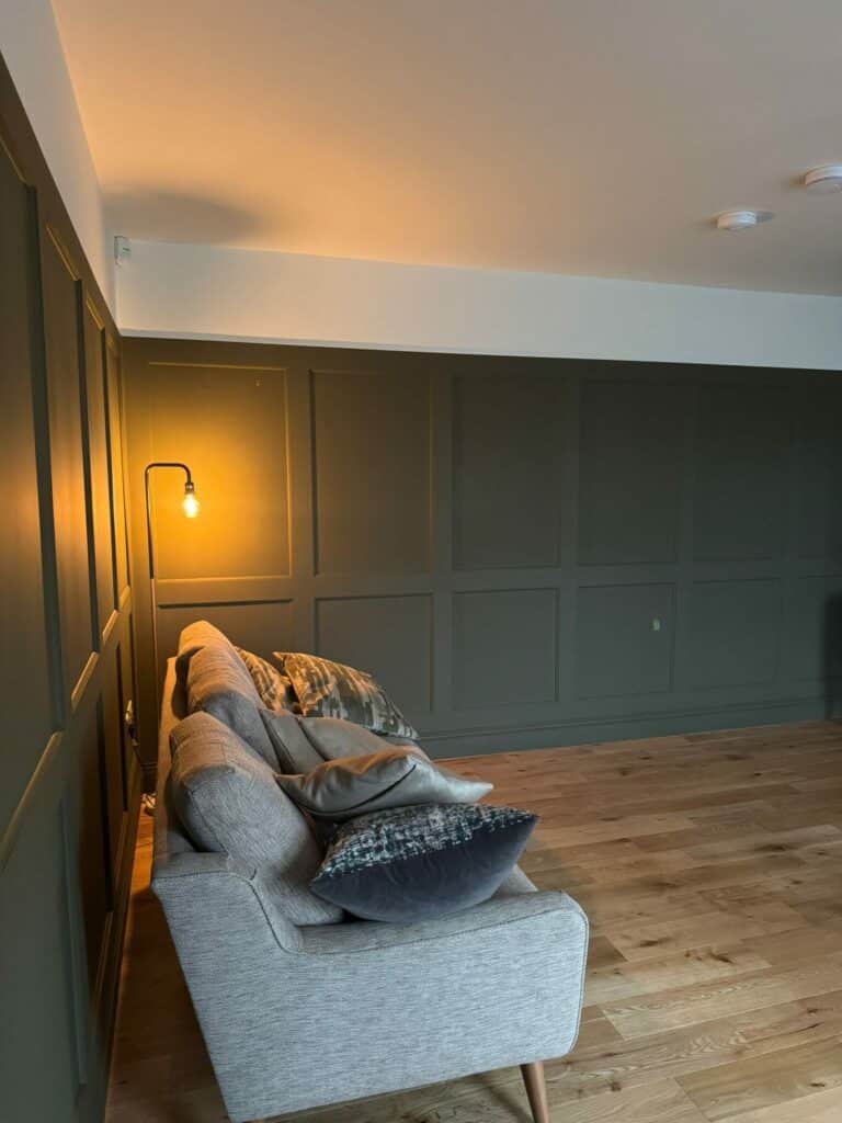 Cozy living room with gray sofa, decorative pillows, wooden floor, and a warm wall lamp for ambient lighting.