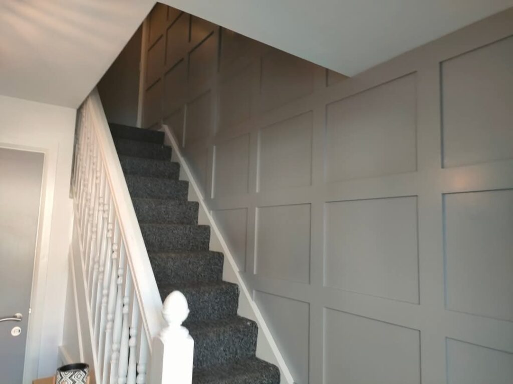 Carpeted staircase with white banister, gray paneled wall, and a partially visible door.