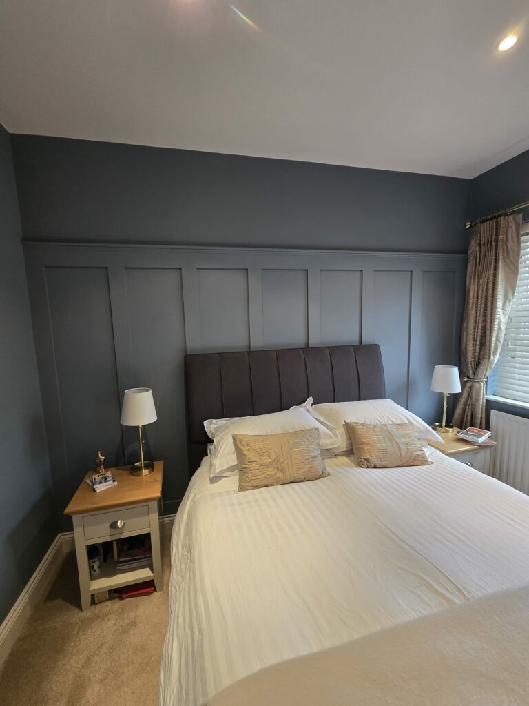 Modern bedroom with dark accent wall, double bed, white linens, decorative pillows, and bedside tables with lamps.