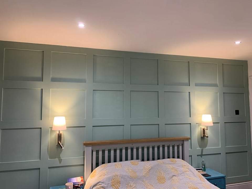Bedroom with light green paneled wall, wooden bed, and two wall sconces.