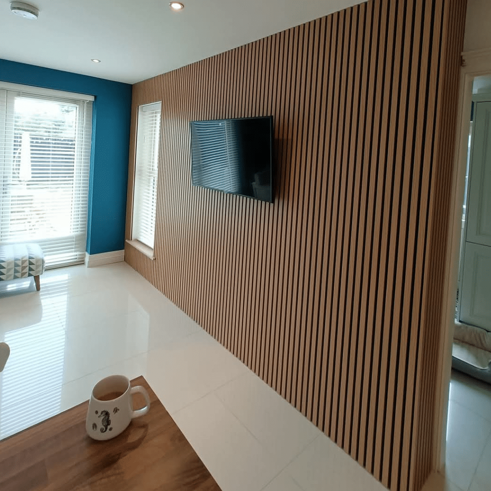 Modern room with wooden slat wall, mounted TV, blue accent wall, and mug on a wooden table.