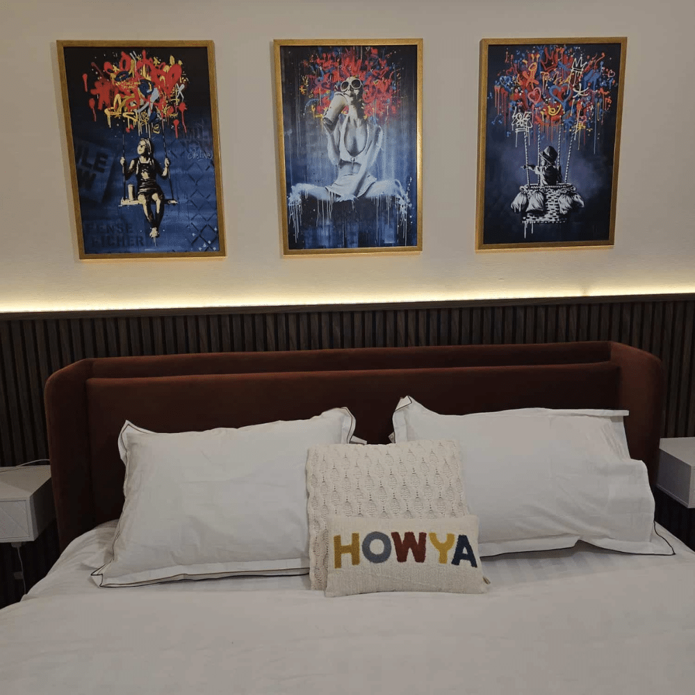 Bedroom with a modern headboard, decorative pillows, and three abstract paintings above.