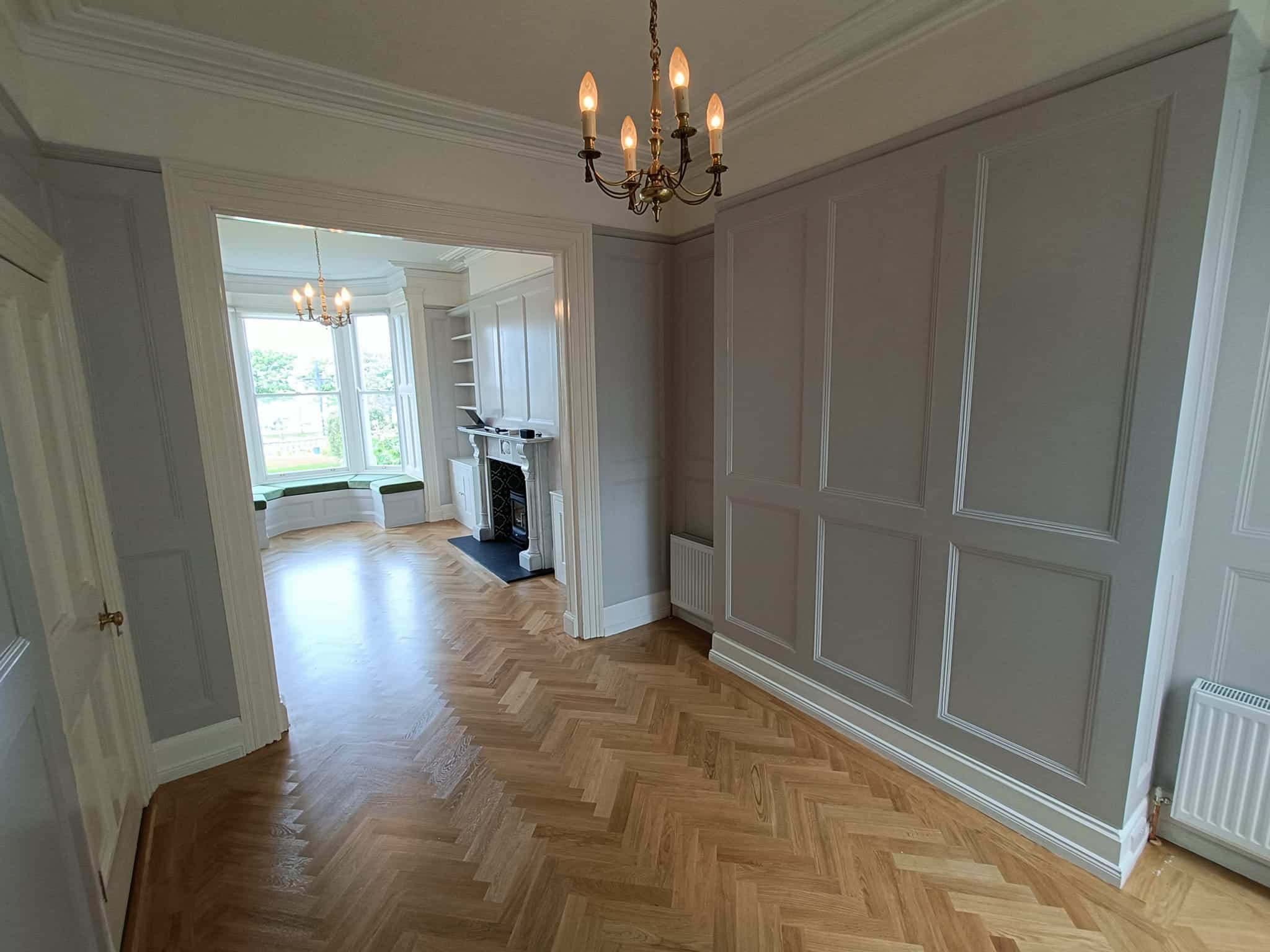 Elegant room with parquet flooring, chandelier, fireplace, and large windows with window seating.