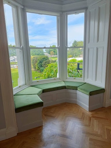 Bay window with green cushioned seating and view of garden.