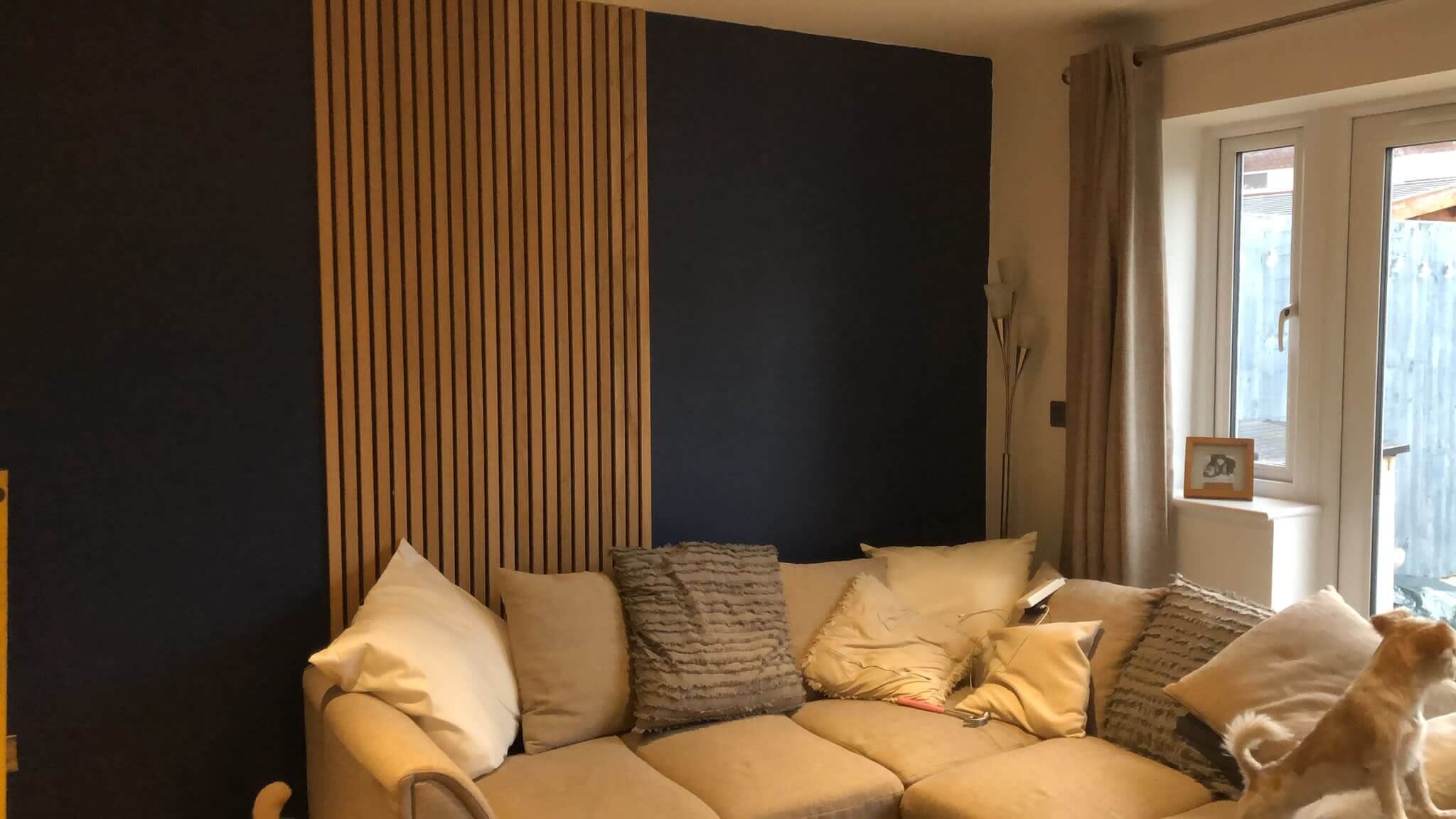 Cozy living room with beige sectional sofa, textured pillows, wood paneling, and a dog looking out the window.